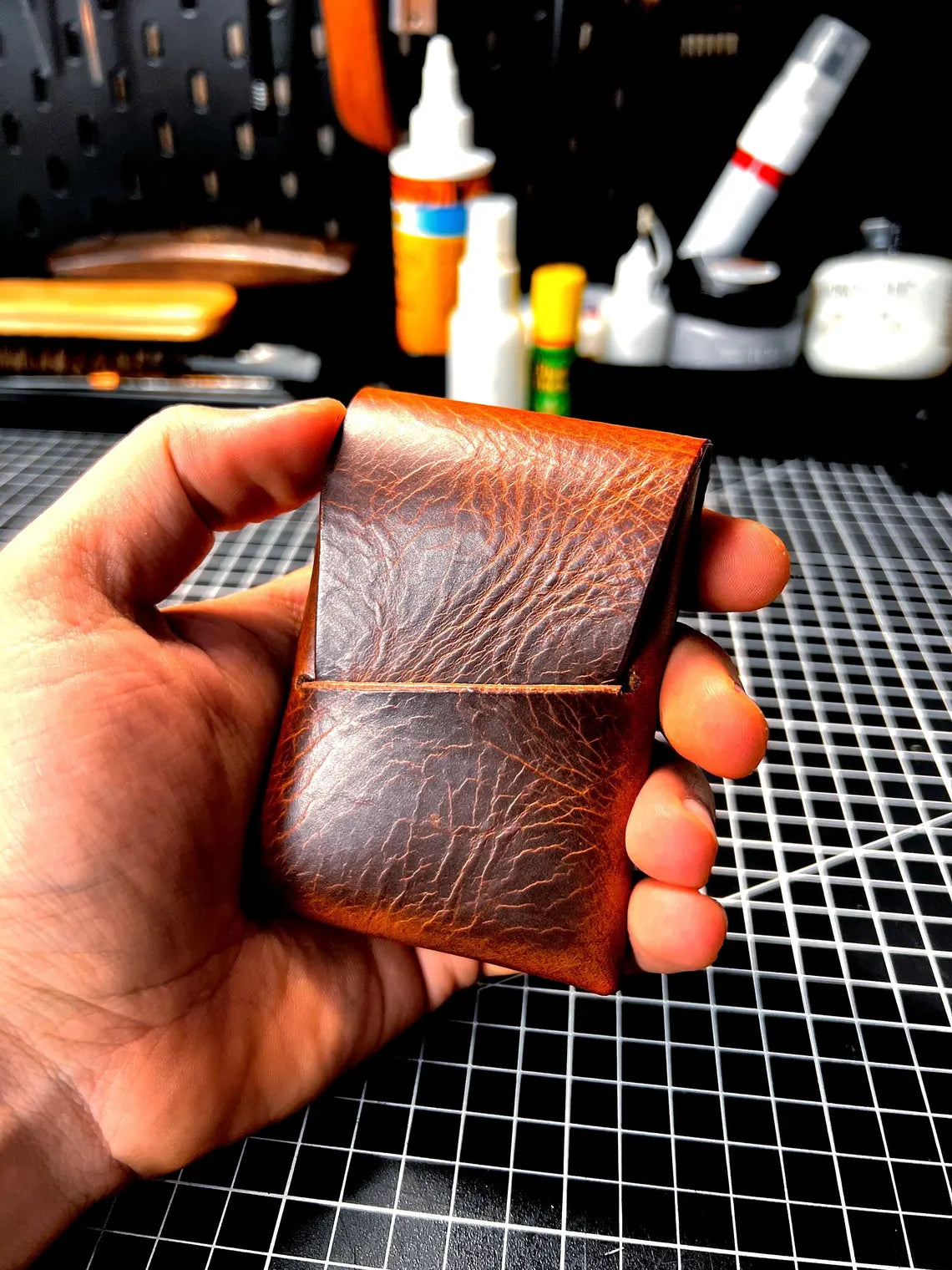 Hand holding a brown leather wallet with a workshop in the background